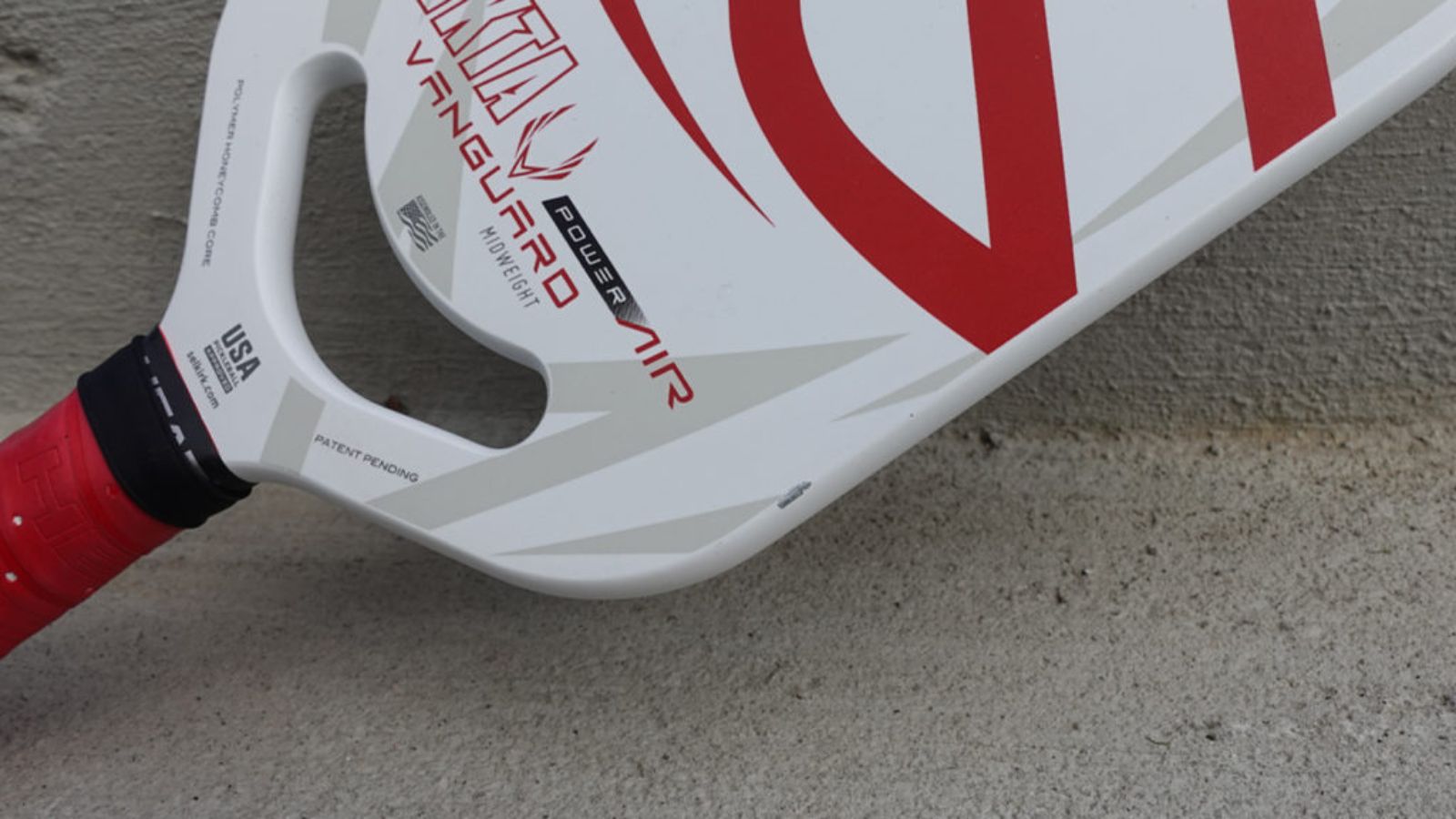 Cận cảnh vợt pickleball Selkirk Vanguard Power Air với thiết kế màu đỏ và trắng, có dòng chữ 'USA' và 'patent pending' trên tay cầm, đặt trên bề mặt bê tông.
