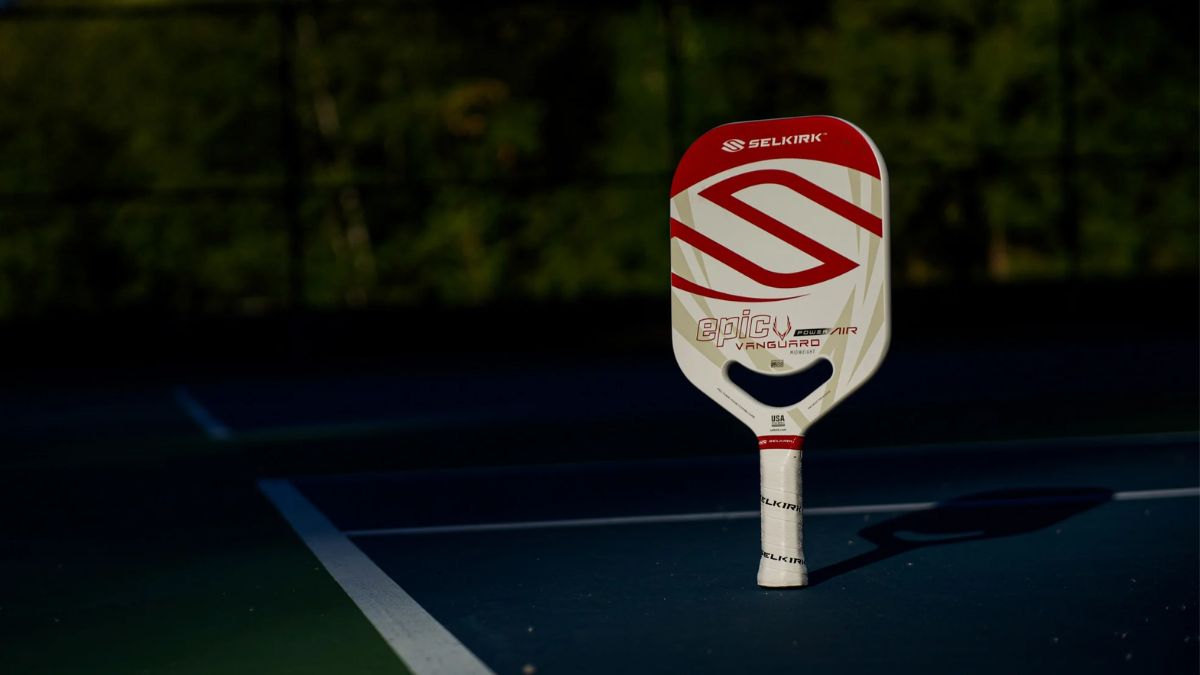 Vợt pickleball Selkirk Epic Vanguard Power Air màu trắng và đỏ, được dựng đứng trên sân chơi với ánh sáng nhẹ