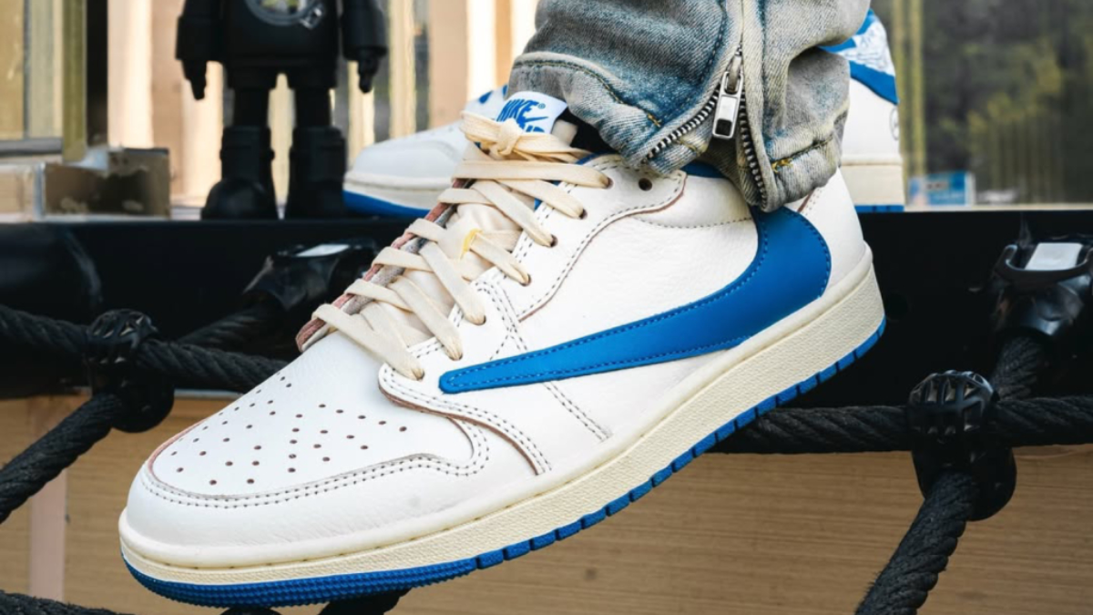 Travis Scott x Fragment x Air Jordan 1 Low OG voi logo Swoosh nguoc va mau xanh Military Blue tren nen da trang.
